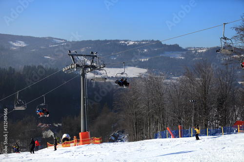 Wyciąg krzesełkowy, narciarze zjeżdżają z góry po śniegu.