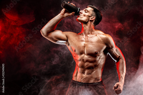 Photography Muscular man with protein drink in shaker over dark smoke background