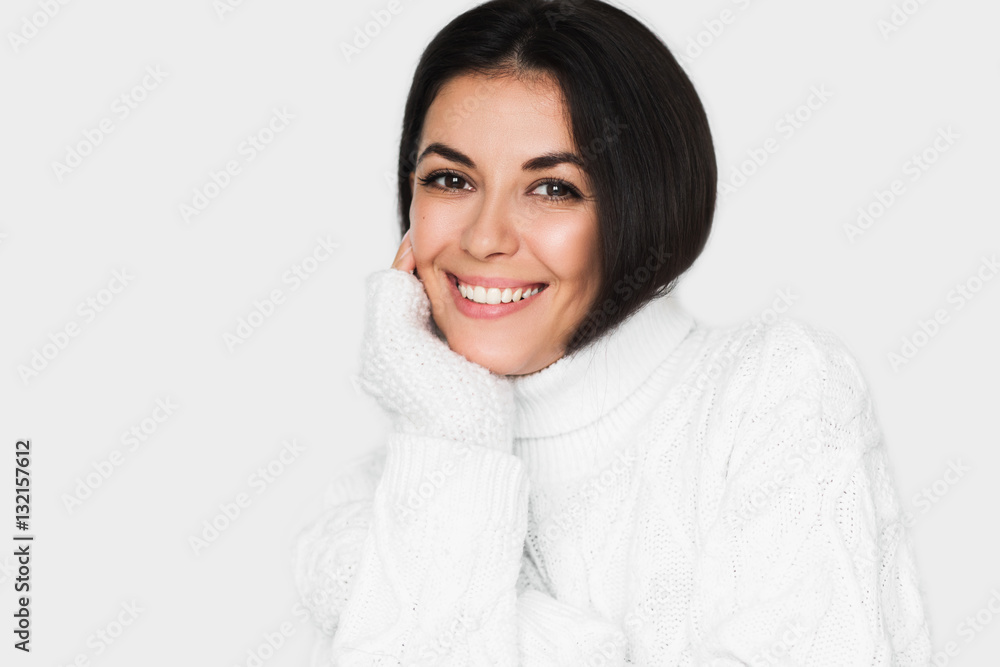Beautiful young happy woman looking pensive and happy in white sweater on light grey background. Pretty brunette with healthy teeth smile woman studio portrait. Positive mood. Beautiful young happy woman looking pensive and happy in white sweater on light grey background. Pretty brunette with healthy teeth smile woman studio portrait. Positive mood.