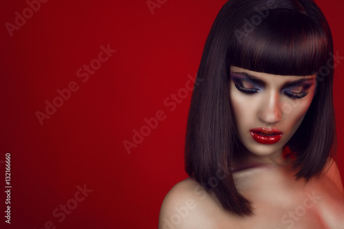 Portrait of beautiful girl with bright colorful provocative make-up, dark smooth shining hair and naked shoulders looking down. Isolated on red background. Copy-space. Close up. Studio shot