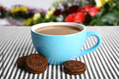 Cup of aromatic coffee on table against blurred floral background. Flower bar concept