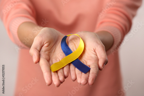 Close up view of female hands holding blue-and-yellow ribbon. Down syndrome concept