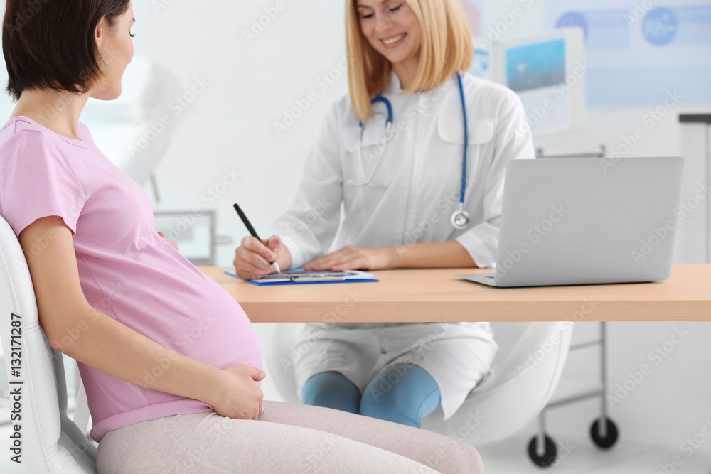 Fototapeta premium Gynecologist writing prescription to pregnant woman in hospital