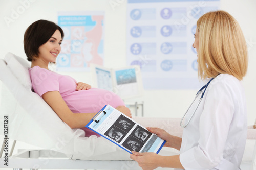 Pregnant woman visiting doctor. Gynecologist holding clipboard with ultrasound photo