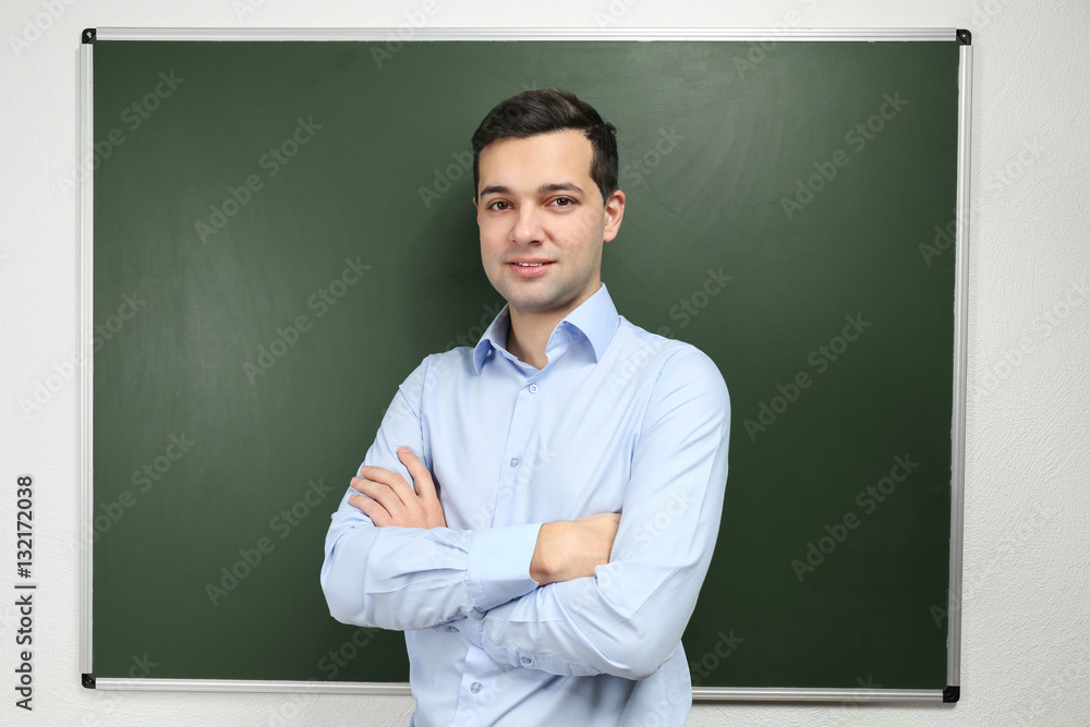 Handsome young teacher near blackboard in classroom