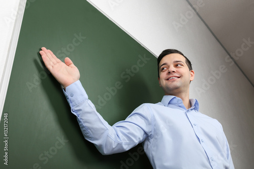 Handsome young teacher standing near blackboard in classroom
