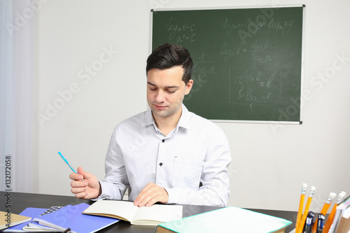 Handsome young teacher sitt...