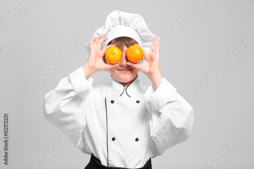 Cute boy in chef uniform on light background