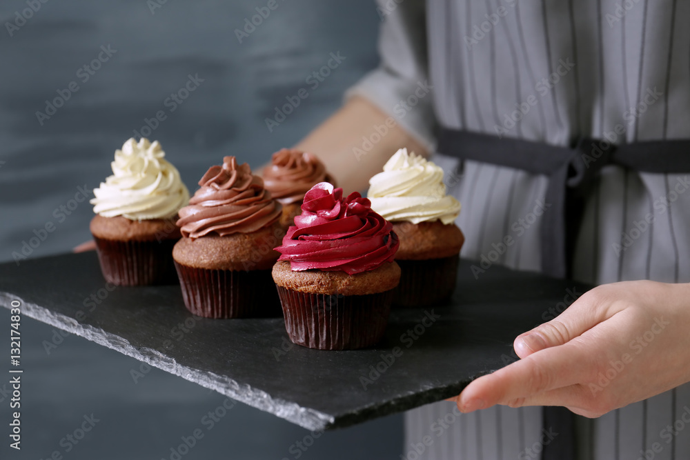 Woman holding slate plate with tasty cupcakes, close up