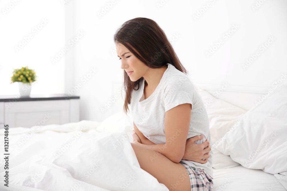 Young woman with stomach ache sitting on bed Young woman with stomach ache sitting on bed