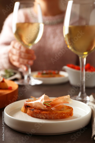 Woman sitting at table with glass of wine and tasty bruschetta