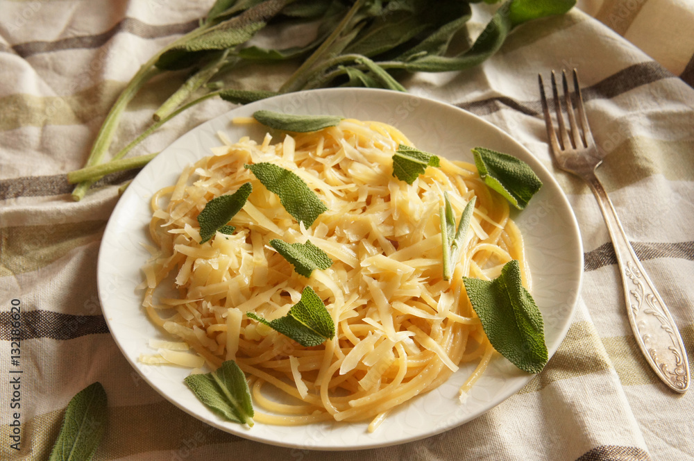 Spaghetti in round white plate with cheese and sage plant on the white and green tablecloth Spaghetti in round white plate with cheese and sage plant on the white and green tablecloth