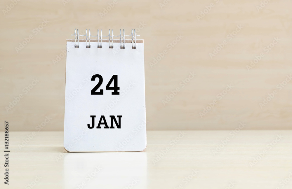 Closeup surface note book with black 24 jan word in page on blurred brown wood desk and wood wall textured background with copy space under window light
