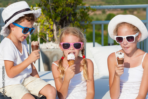 Three happy children eating ice cream near swimming pool at the
