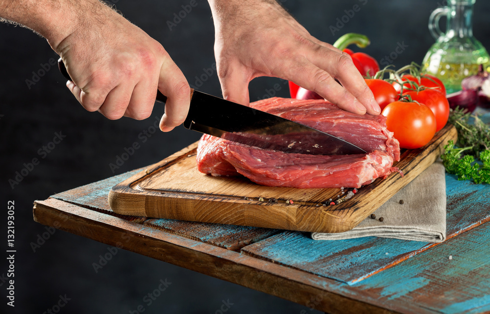 Butcher cutting beef meat on a wooden table on the dark background Butcher cutting beef meat on a wooden table on the dark background