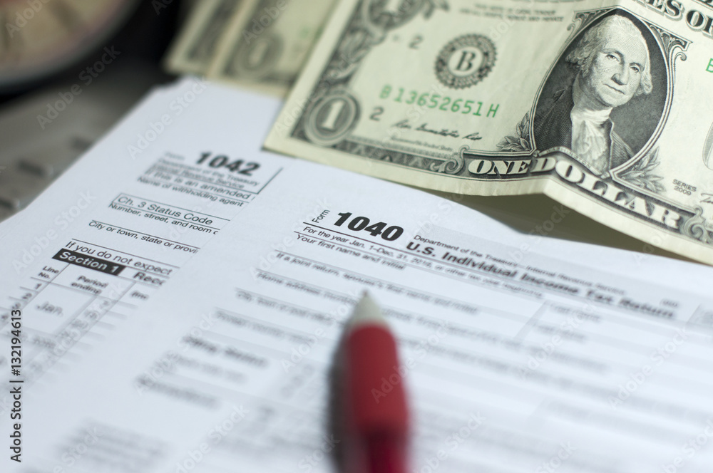 Tax Season: 1040 U.S. Individual Income Tax Return Form horizontal top view with an office laptop and blue calculator as background together with a red white pen preparation on taxation as foreground Tax Season: 1040 U.S. Individual Income Tax Return Form horizontal top view with an office laptop and blue calculator as background together with a red white pen preparation on taxation as foreground