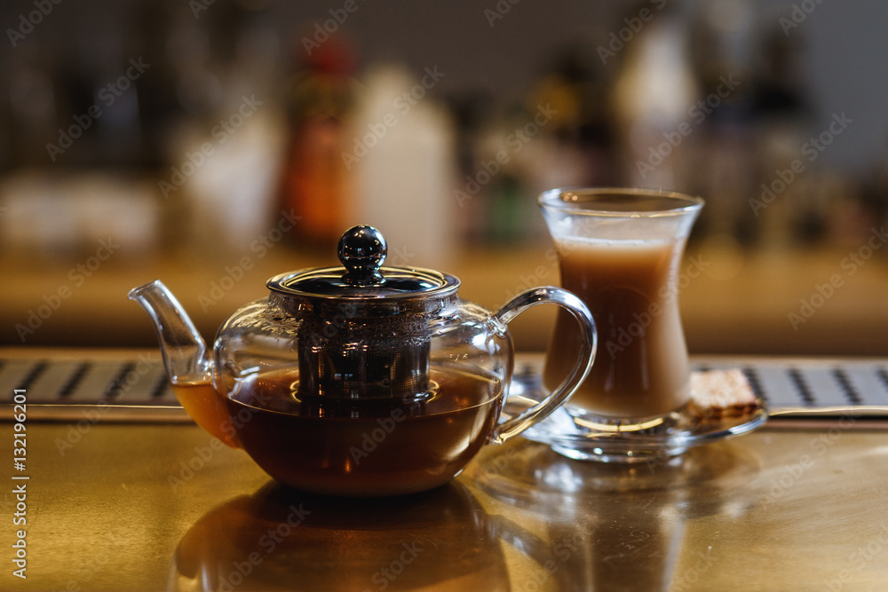 An underexposed lifestyle horizontal image of a teapot with hot alcoholic cocktail on a black tea basis. Wooden bar stand of a restaurant. An underexposed lifestyle horizontal image of a teapot with hot alcoholic cocktail on a black tea basis. Wooden bar stand of a restaurant.