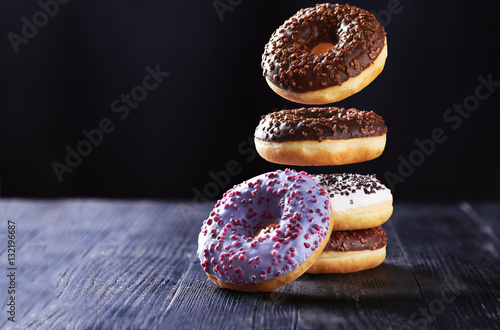 Donut with chocolate icing in motion falling on a tasty donuts with blue, chocolate and vanilla icing on a dark wooden background.