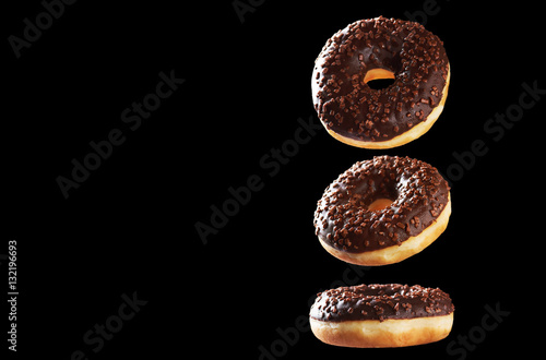 Three tasty chocolate donuts in motion isolated on black