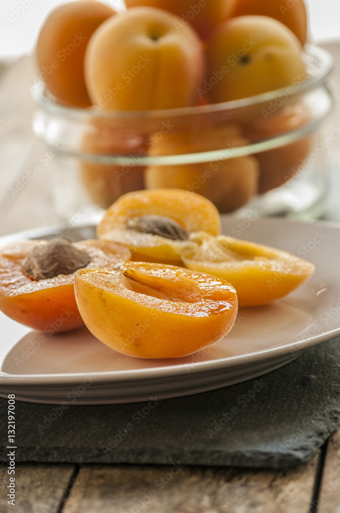 Whole orange apricots with red blush, from above, space for text. Open apricot with stone and leaves. On rustic white wood.
