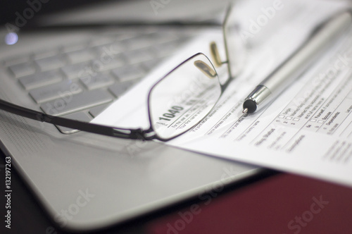Tax Season: 1040 U.S. Individual Income Tax Return Form horizontal top view with an office laptop and blue calculator as background together with a red white pen preparation on taxation as foreground