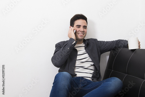 male young taking coffee and talking by the phone phone in the apartment