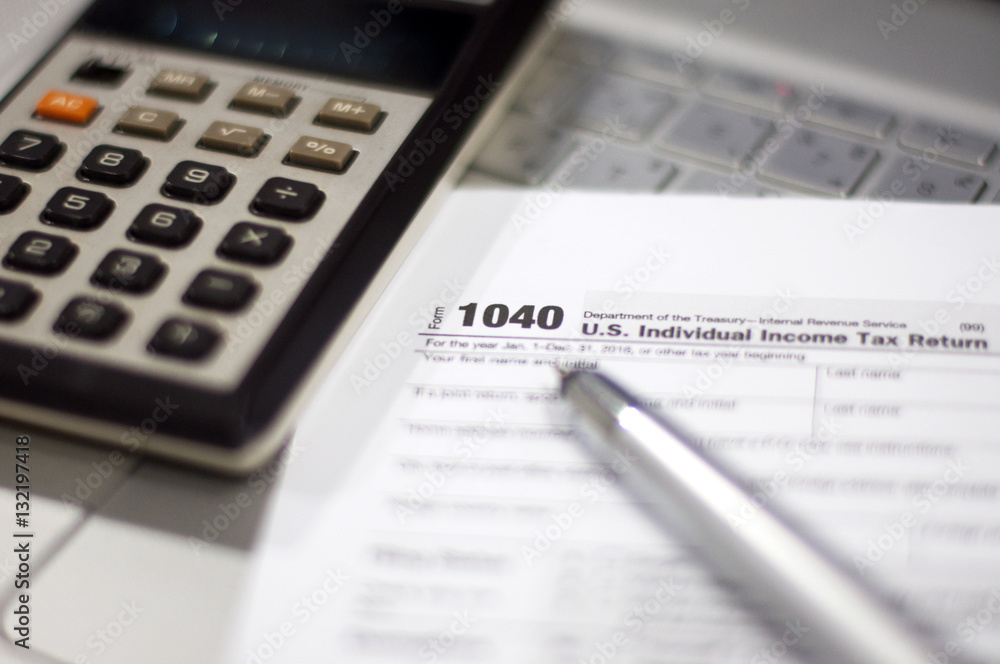 Tax Season: 1040 U.S. Individual Income Tax Return Form horizontal top view with an office laptop and blue calculator as background together with a red white pen preparation on taxation as foreground Tax Season: 1040 U.S. Individual Income Tax Return Form horizontal top view with an office laptop and blue calculator as background together with a red white pen preparation on taxation as foreground