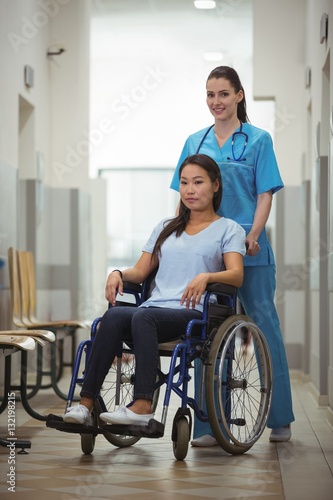 Female nurse assisting patient on wheelchair in corridor