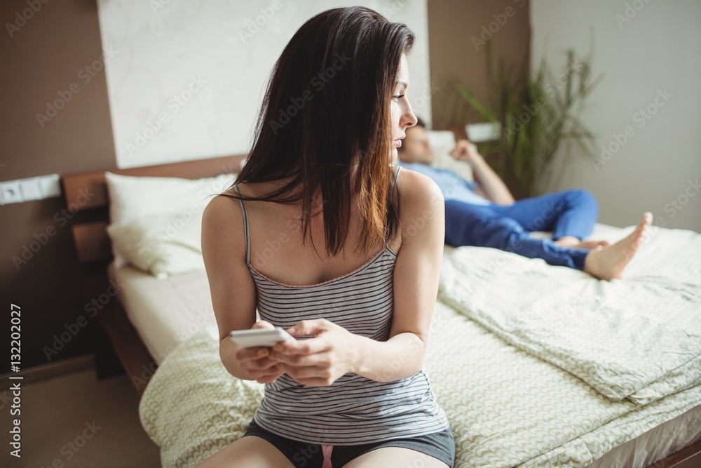 Fotografie Woman using mobile phone while man sleeping on bed