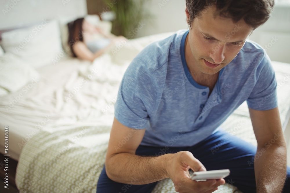 Man using mobile phone while woman sleeping on bed Man using mobile phone while woman sleeping on bed