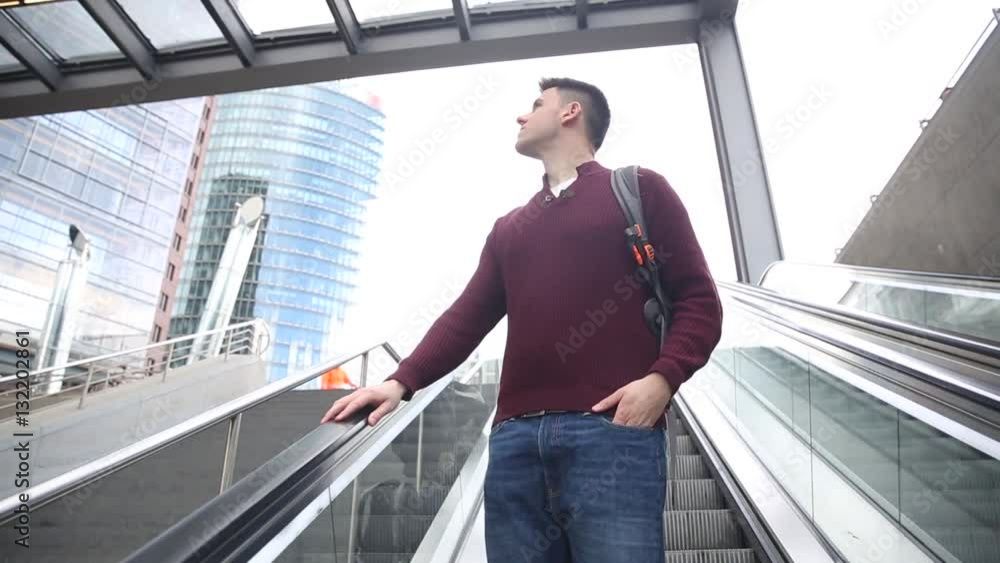 Young man on the escalator. Caucasian boy in the city taking the escalator and looking around. He is carrying a backpack. City life and travel concepts Young man on the escalator. Caucasian boy in the city taking the escalator and looking around. He is carrying a backpack. City life and travel concepts