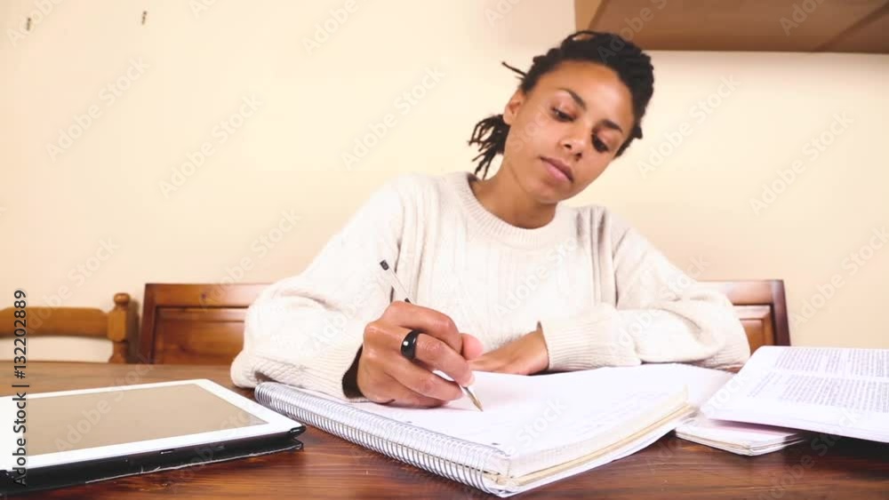 Beautiful mixed race woman studying or working at home. Black girl with dreadlocks alone writing and reading on a digital tablet Beautiful mixed race woman studying or working at home. Black girl with dreadlocks alone writing and reading on a digital tablet