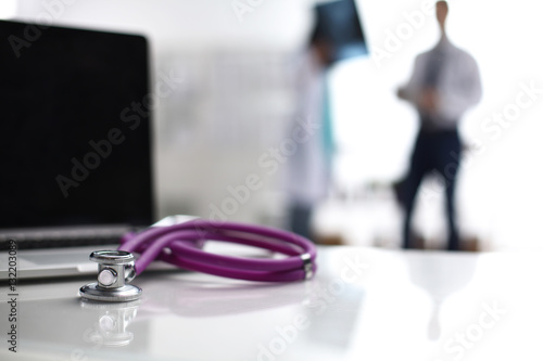 Laptop and stethoscope on the desk , doctors standing in the background photo