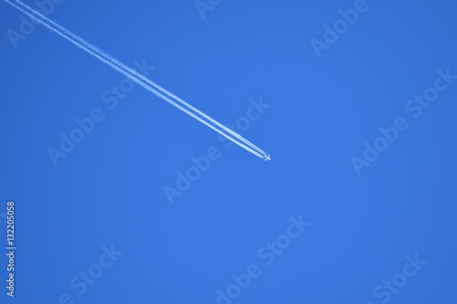 Flugzeug hinterlässt Kondensstreifen im strahlend blauen, wolkenfreien Himmel.