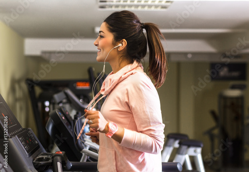 Girl running on the treadmill and listening music at the gym.