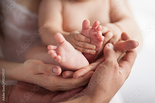 Baby's feet in mother's and father's hands. Close up.
