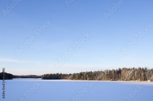 Wintry landscape from Finland. Image taken on a cold morning. Sun is about to rise and creates shadows on the lake ice. Snow covered landscape. Copy space