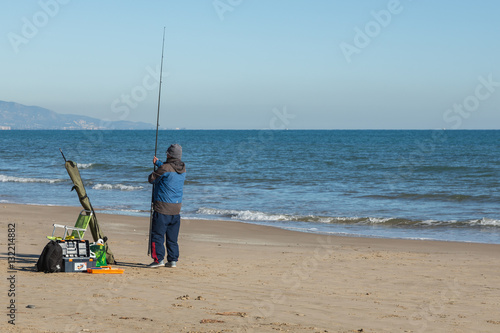 Man fiskar med kastspö på en sandstrand vid havet photo