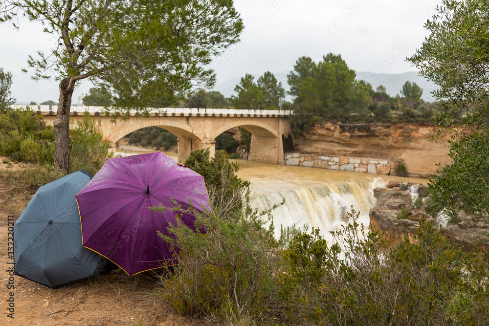 Personer gömda bakon paraplyer framför bro över en flod och vattenfall