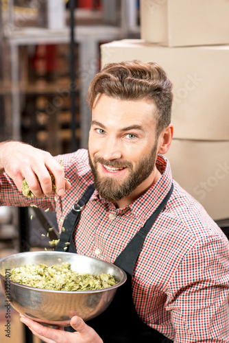 Brewer with green hops dressed in apron and checkered shirt at the manufacturing. Epertising quality of beer ingredients