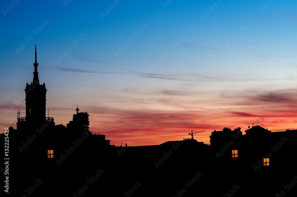 Night cityscape. Silhouettes of houses with tower and luminous windows. Red sunset sky.