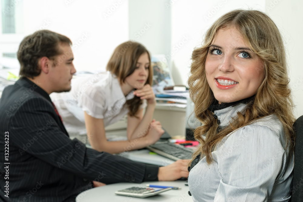 Portrait of office worker woman sitting, looking at camera, colleagues at background. Portrait of office worker woman sitting, looking at camera, colleagues at background.