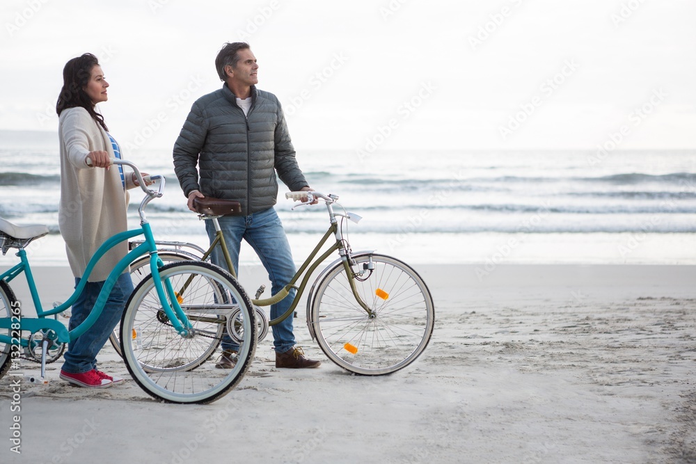 Fototapeta premium Couple standing with bicycle on beach