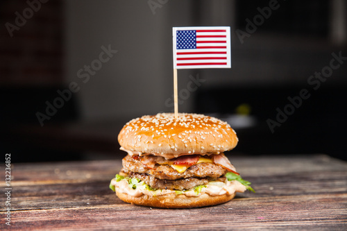 Tasty grilled beef burger with lettuce, ketchup, onion rings, chili and mayonnaise served on pieces of brown paper on a rustic wooden table of counter, with copyspace