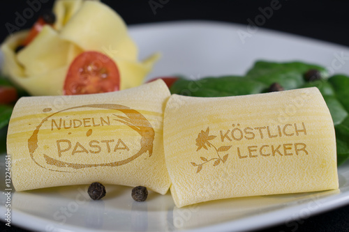 Auf einem weißen Teller befinden sich im Vordergrund 2 Nudeln mit Schriftzug - Nudeln Pasta und Köstlich Lecker