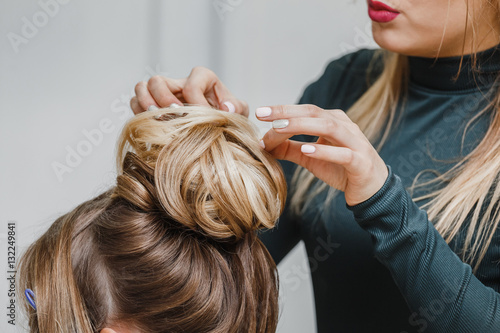 Hairdresser makes upper bun hairstyle close-up on brown hair of beautiful woman