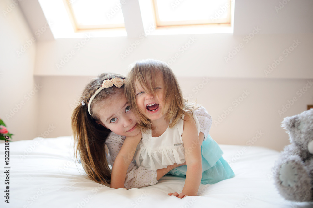 On a big bed two little sisters lie in an embrace. On a big bed two little sisters lie in an embrace.