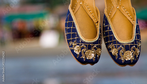 Blue colored traditional ethnic Indian jutis (women's shoes) with embroidery on a beach in north Goa, India in the evening with a blurry backgound photo