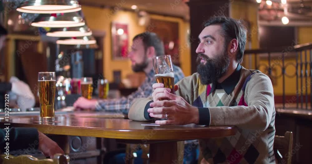 Male friends talks and drinks beer at pub bar 4k video. Men taste lager from glasses, bartender and other guests at the background. Male friends talks and drinks beer at pub bar 4k video. Men taste lager from glasses, bartender and other guests at the background.