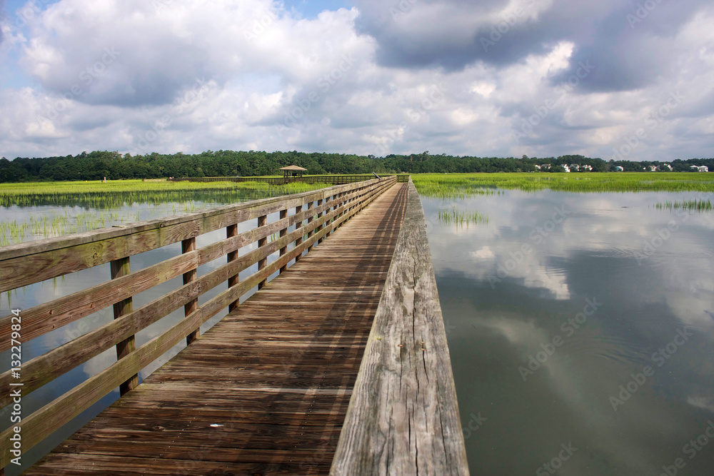 Huntington Beach State Park, South Carolina, USA. View from the wooden boardwalk on the expansive salt marsh. Landscape with cloudy blue sky reflected in the water.
